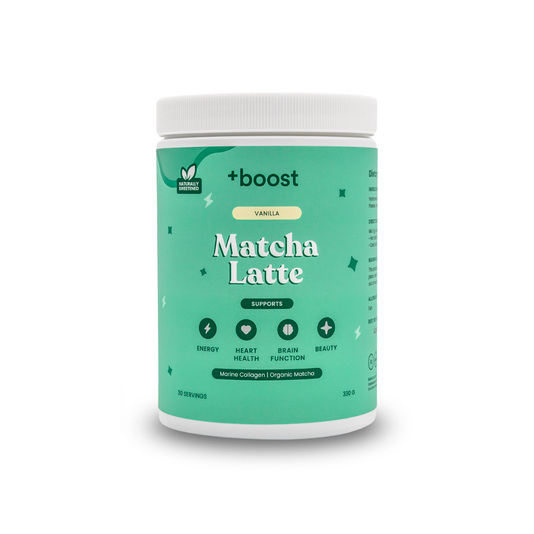 Creamy +boost Matcha Latte in a glass mug with frothy top, featuring vibrant green matcha powder, on a wooden surface.