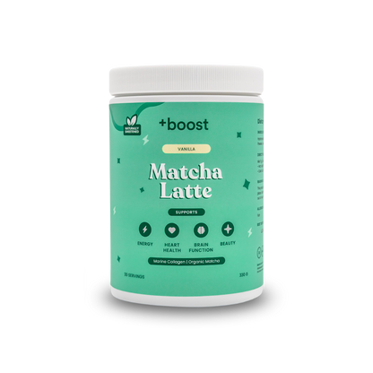 Creamy +boost Matcha Latte in a glass mug with frothy top, featuring vibrant green matcha powder, on a wooden surface.