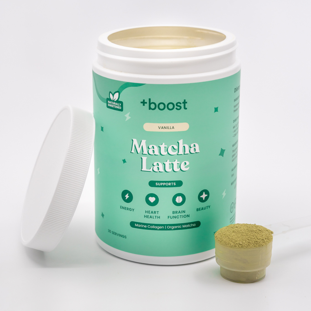 Creamy +boost Matcha Latte in a glass cup, topped with foamed milk and vibrant green matcha powder on a wooden table.