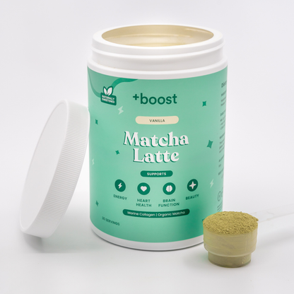 Creamy +boost Matcha Latte in a glass cup, topped with foamed milk and vibrant green matcha powder on a wooden table.