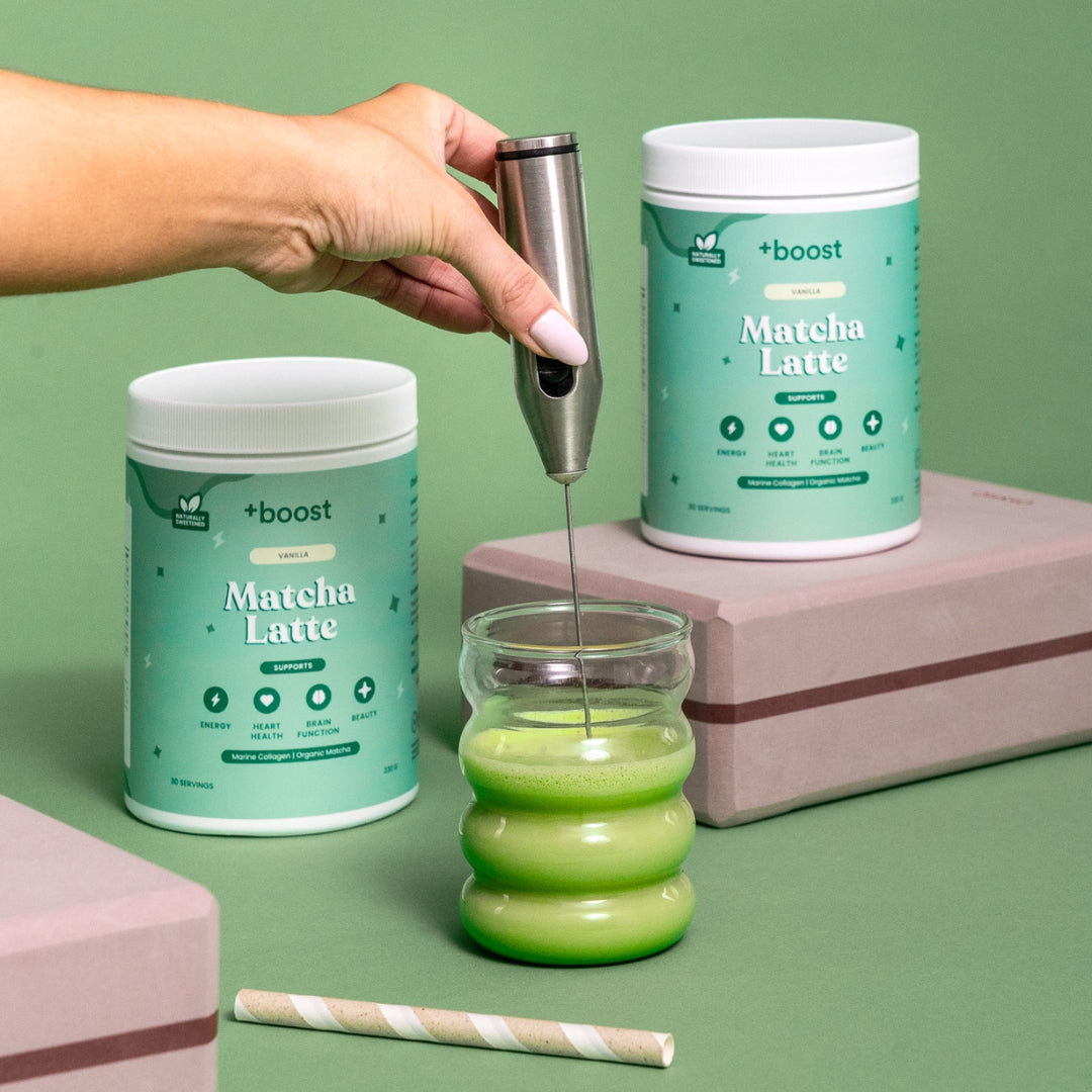 Creamy +boost Matcha Latte in a glass cup with frothy surface, featuring vibrant green matcha powder on top.