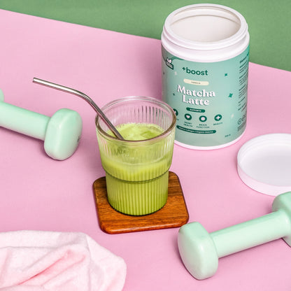 Creamy +boost Matcha Latte in a glass cup with frothy green matcha powder on top, served in a cozy setting.